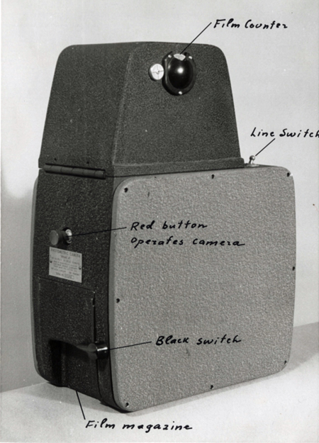 Black-and-white photo of a metal photometric camera with handwriting pointing out specific features: film counter, line switch, red button operates camera, black switch, film magazine.