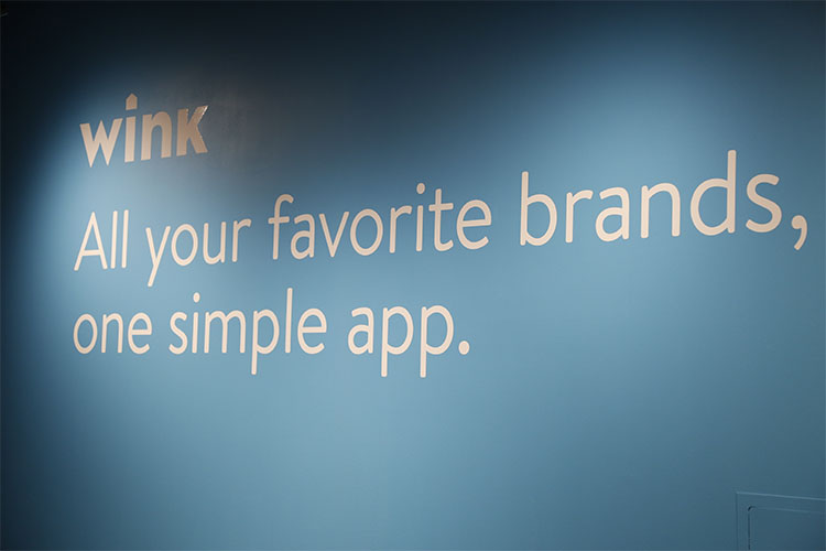 Wink brand logo painted on a wall with the tagline, "All your favorite brands, on one simple app."