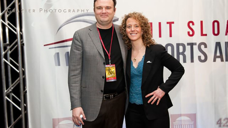 Daryl Morey and Jessica Gelman pose in front of a banner for the MIT Sloan Sports Analytics Conference