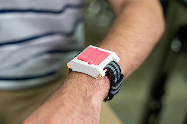 A man models the prototype on his wrist. It is a square box with a hinged lid attached to a watch band.
