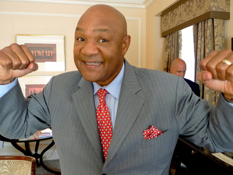 Boxer George Foreman, with arms up and hands clenched as if ready to punch, but with a big grin on his face and wearing a suit
