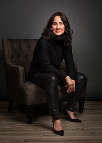 Cynthia Breazeal, sitting in a chair, leaning forward, dressed in black with dark gray background
