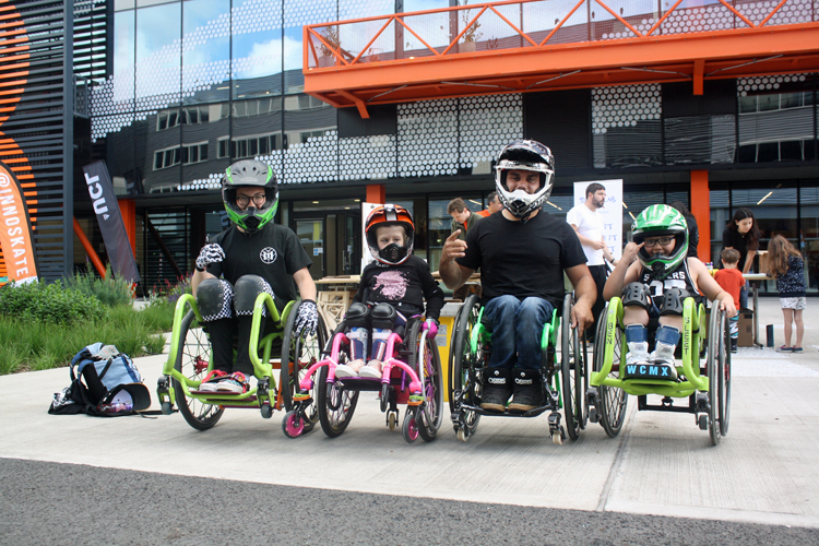 3 children and one man, all in wheelchairs and wearing skateboarding helmets, line up for the camera.