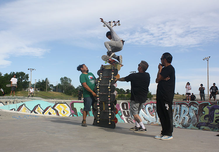 A skater in mid-air jumping over 13 skateboards stacked on horizontal edge.