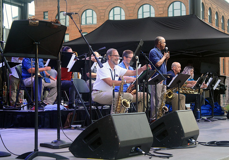 A man speaking into a microphone, standing among orchestra members preparing to play