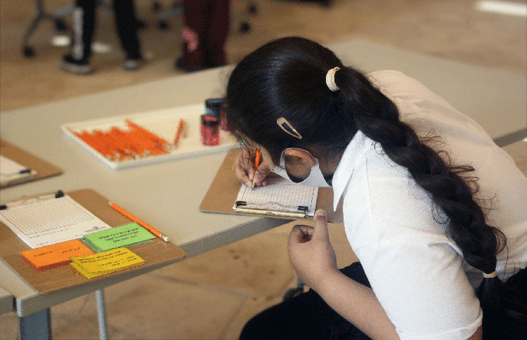 A young girl bends over her sketch pad to draw her invention idea