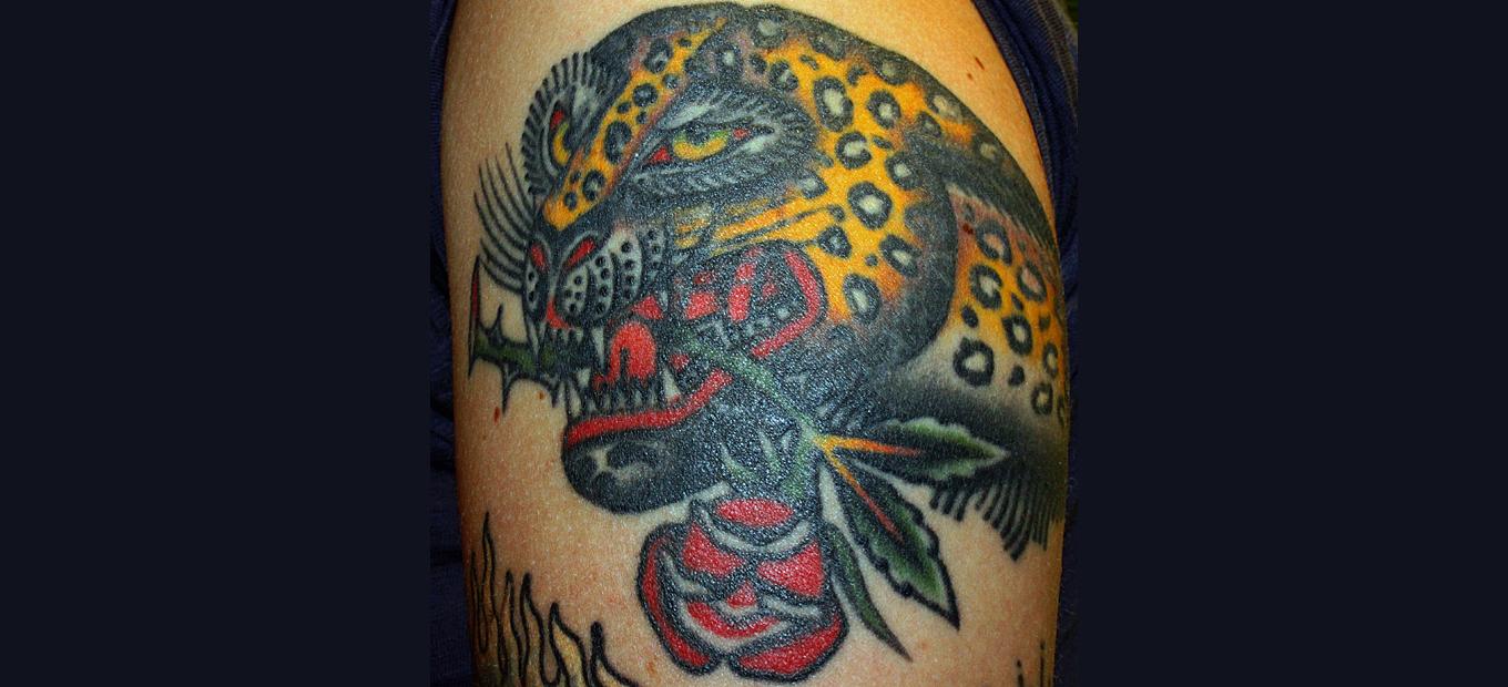 Tattoo of a jaguar holding a rose in its teeth.