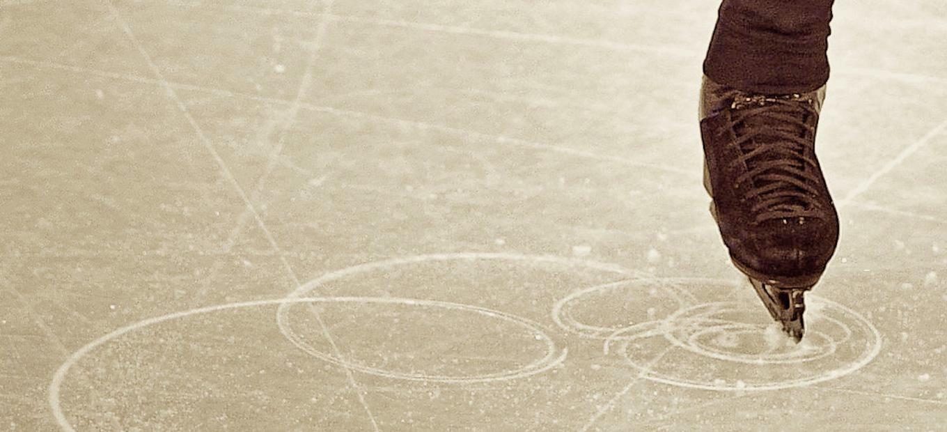 Close-up of a single skater’s foot tracing a figure in the ice.