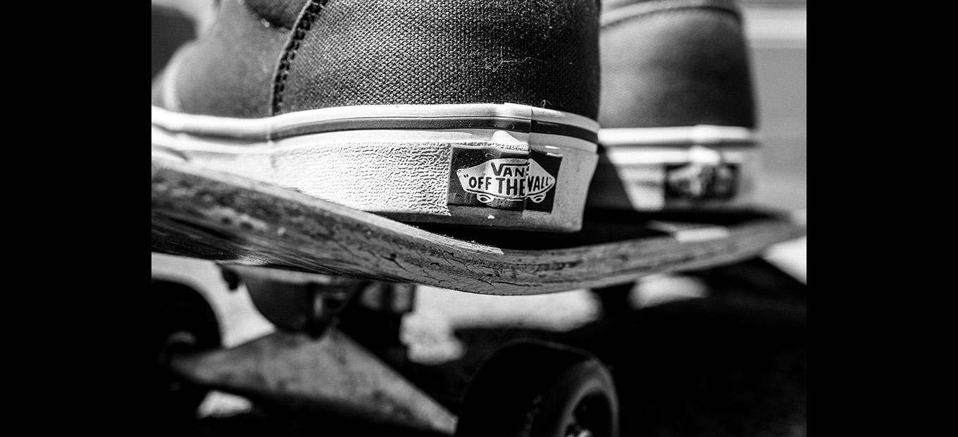 Close-up of the heel of a skateboarder's shoe, showing the Vans label, on a skateboard