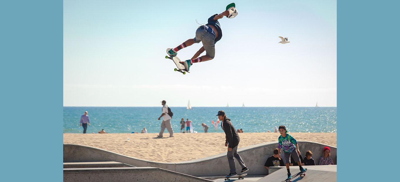 Skateboarders on a ramp at the beach. One is airborne, performing a trick.