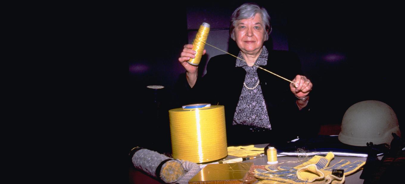 Stephanie Kwolek holding up a thread from a spool of Kevlar