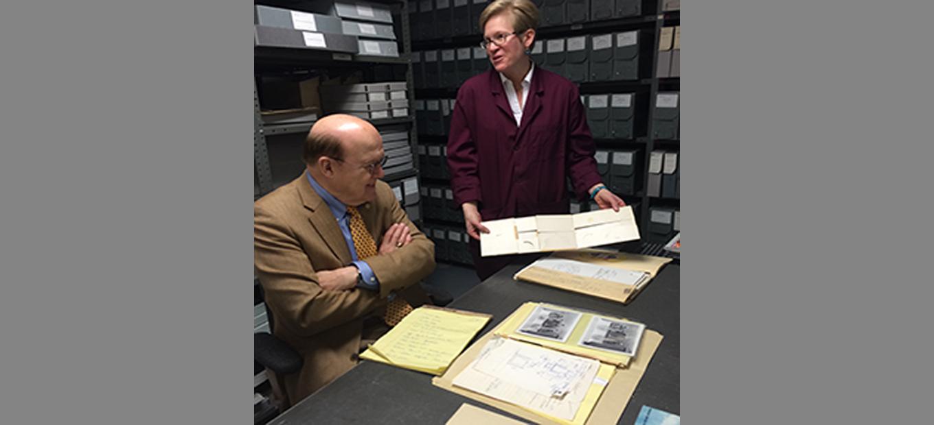 Inventor Manny Villafana seated at table; archivist Alison Oswald standing and showing archival materials to Villafana