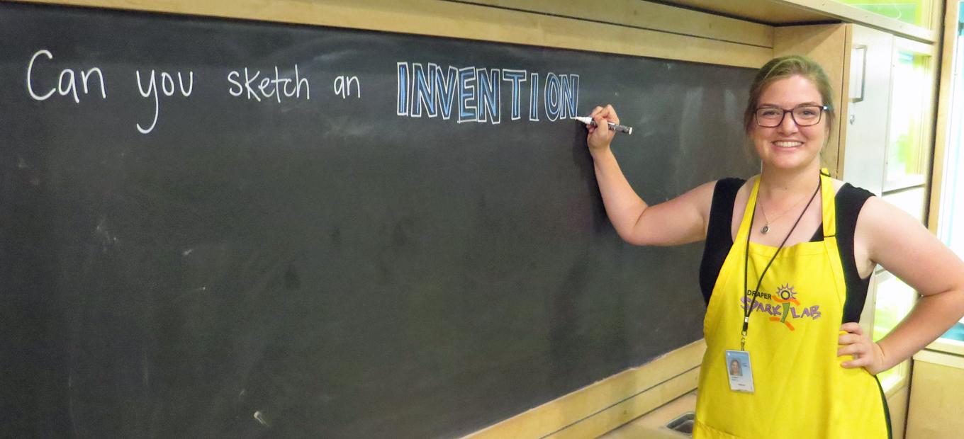 Mary Kate Robbett at blackboard writing Can you Sketch an Invention?