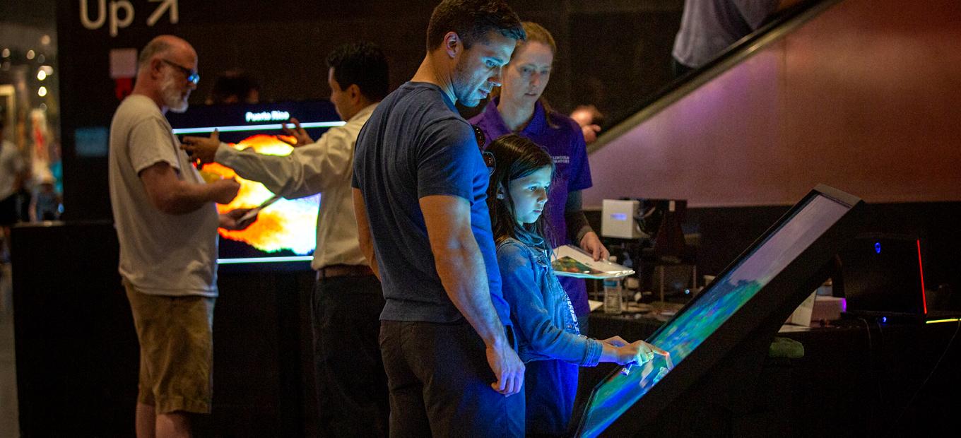 A man, woman, and young girl explore a touchscreen display.
