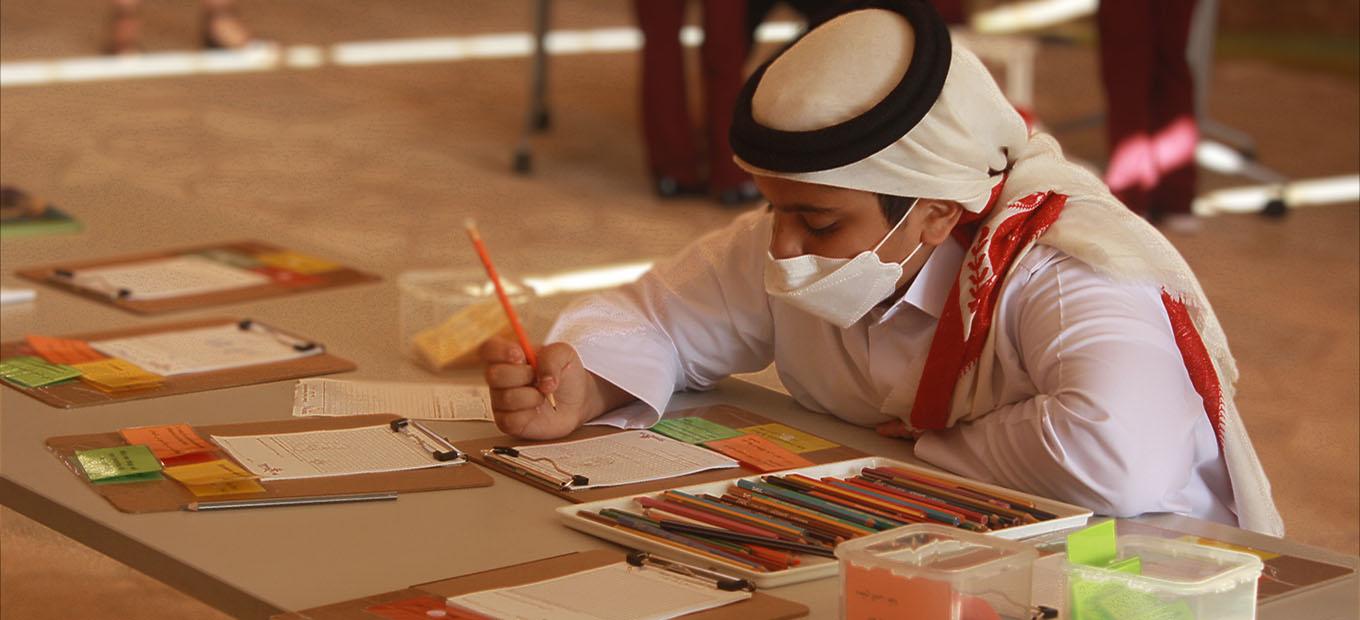 A Qatari boy in traditional dress sketches his invention