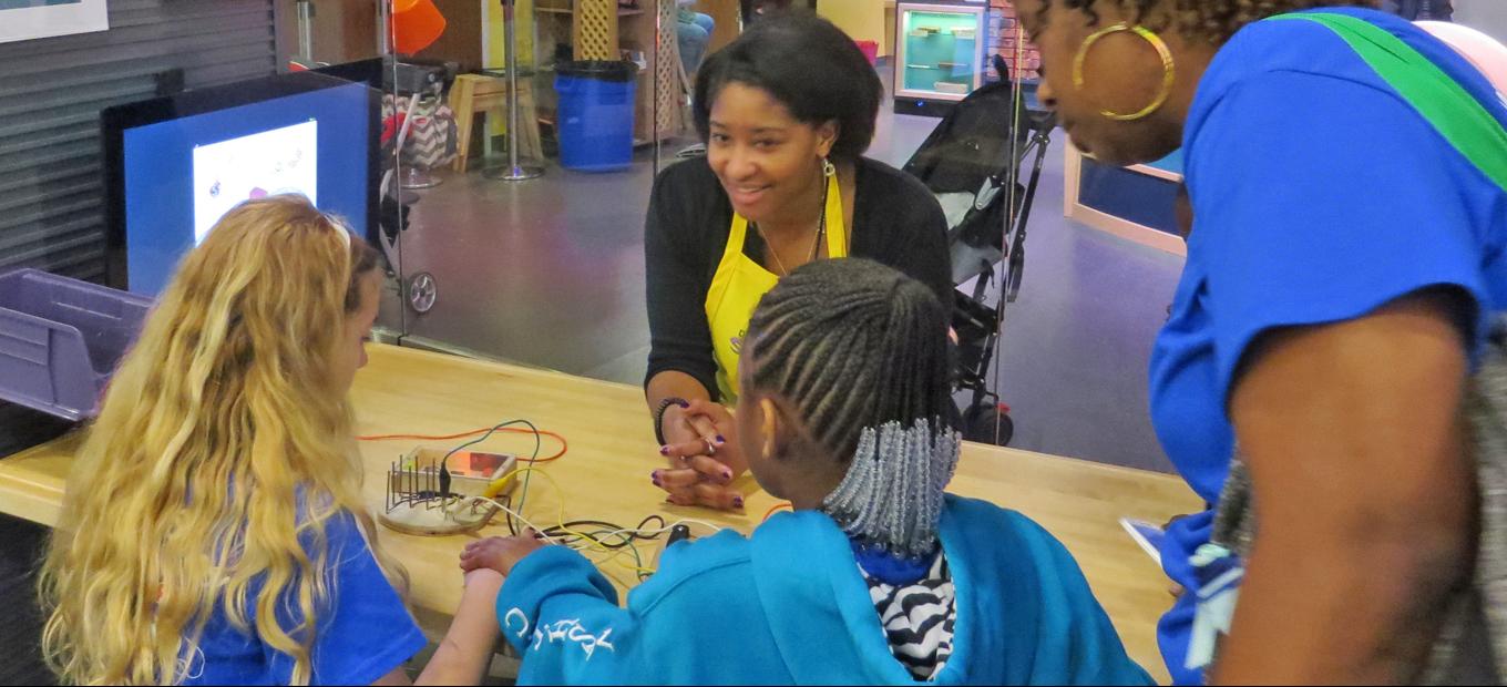 SparkLab volunteer assists two young girls with the Electronic Symphony activity