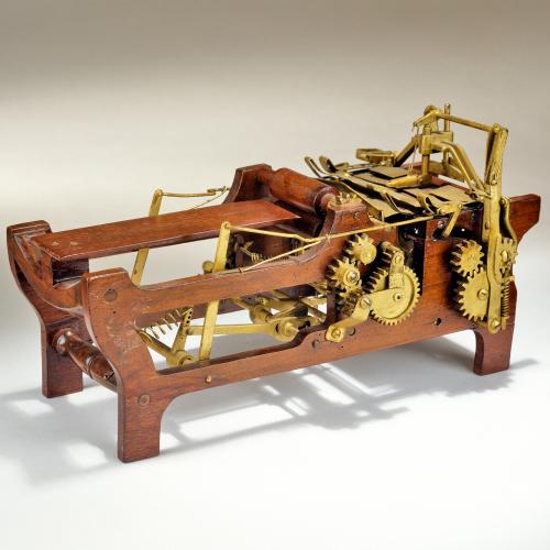 Margaret Knight’s patent model for an improved paper bag making machine shows 2 sets of 3 gears attached by articulated arms and springs to a wooden frame and horizontal bed where the paper is moved through the bag making process.