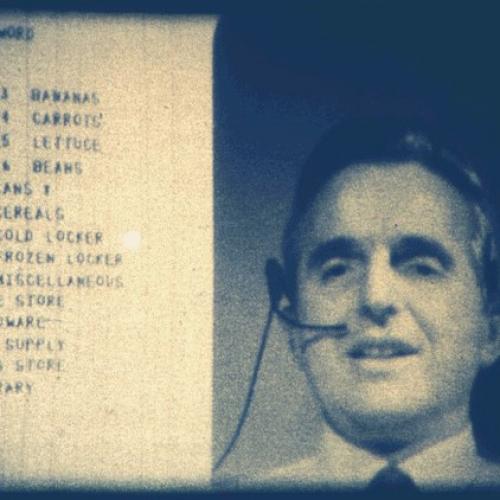Screenshot of Douglas Engelbart presenting the mother of all demos on 9 December 1968. Engelbart wears a headset and his head and shoulders appear on the right side of the screen. Part of a shopping list, including grocery items bananas, carrots, lettuce, beans, and more, is on the left side. 