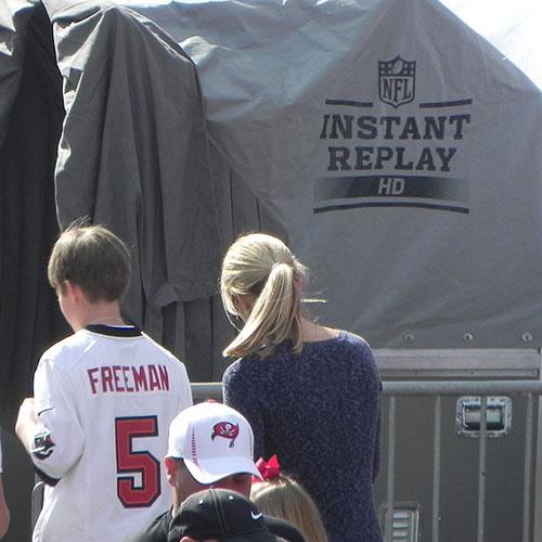 Fans pass walk past a tent labeled NFL Instant Replay
