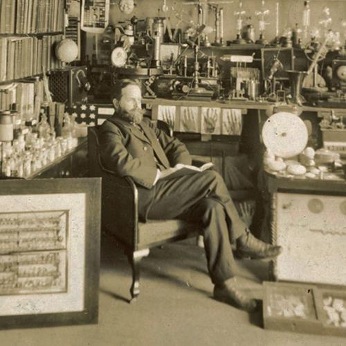 William J. Hammer seated among his large collection of scientific and experimental apparatus