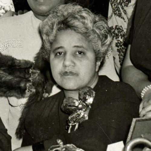 A middle-aged Marjorie Stewart Joyner. The image is cropped from a larger group photo which appears to have been taken at an honorary or celebratory event. Joyner has short, curled hair, is wearing a corsage, and looks straight into the camera. She is not smiling.