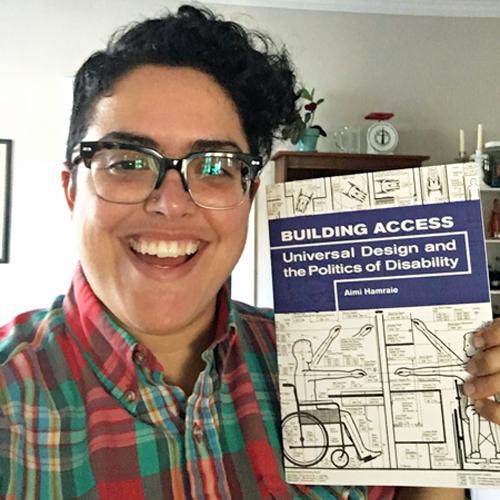 Informal portrait photo of Aimi Hamraie holding her book Building Access.