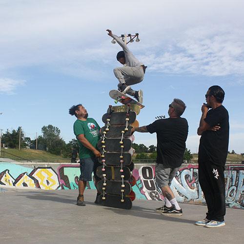 A skater in mid-air jumping over 13 skateboards stacked on horizontal edge