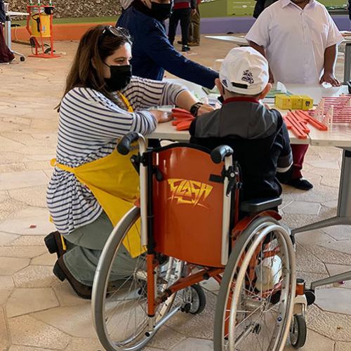 A young child in a wheelchair works with a Spark!Lab facilitator on a stadium-building activity.
